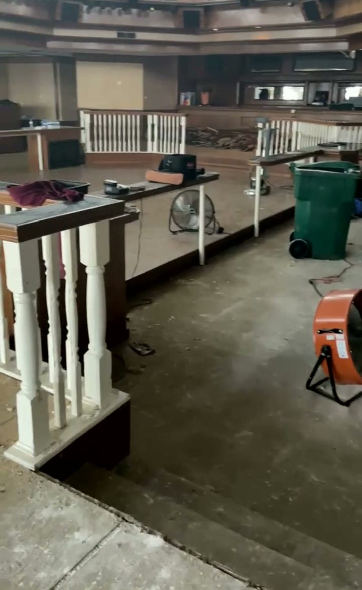 The same room mid-renovation, stripped back with drying fans and debris bins on the bare floor